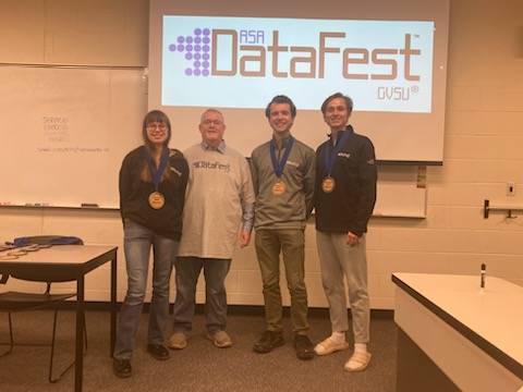 Three students awarded the Collegiality Award and one faculty member pose in front of the DataFest logo.